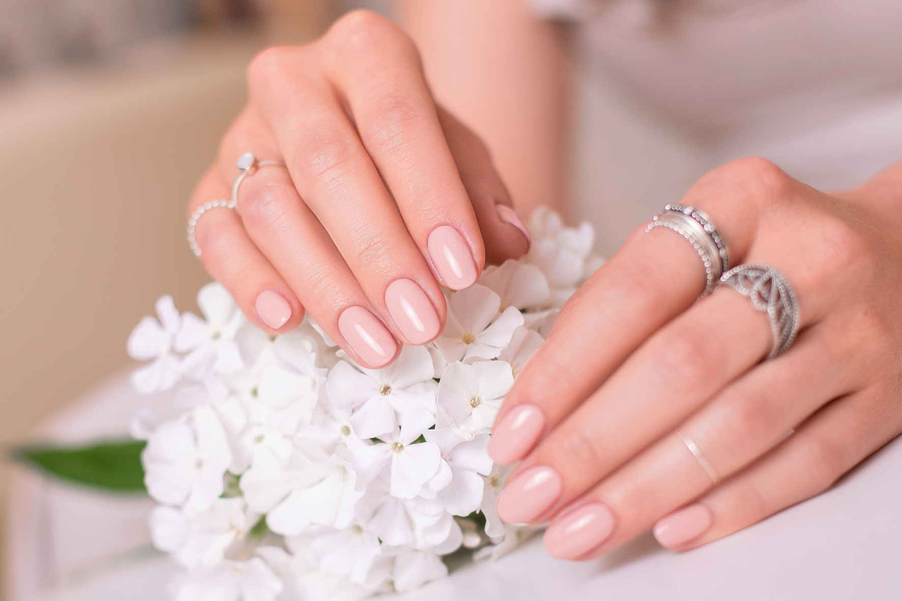 Female hands with romantic manicure nails, nude gel polish, white flowers
